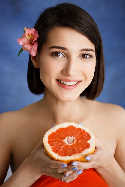 Close up portrait of tender  young woman holding cut orange over blue wall