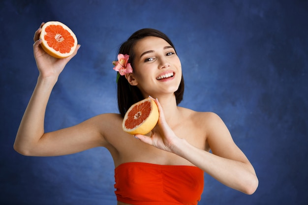 Free photo close up portrait of tender young woman holding cut orange over blue wall