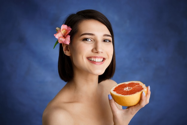 Close up portrait of tender young woman holding cut orange over blue wall