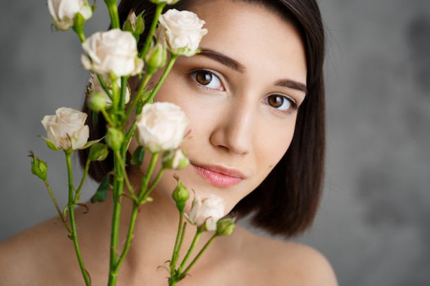 Close up portrait of tender  young woman with flowers over grey wall