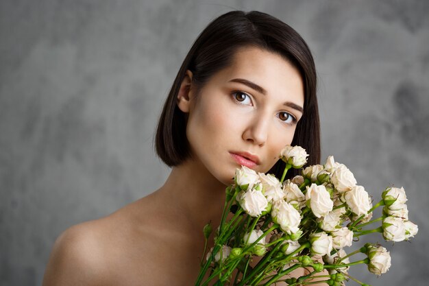 Close up portrait of tender  young woman with flowers over grey wall