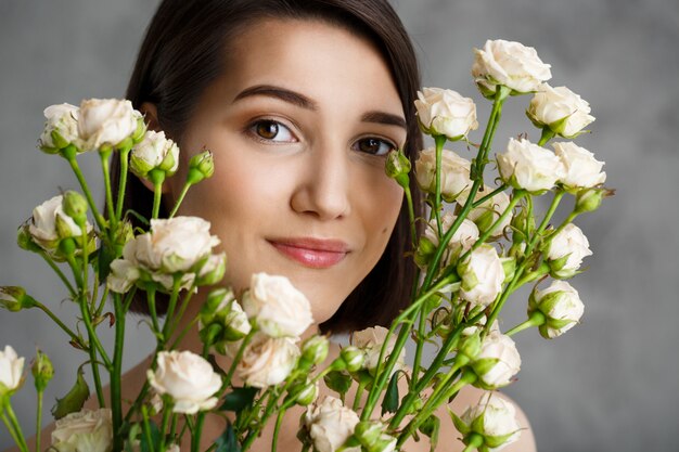 Close up portrait of tender  young woman with flowers over grey wall