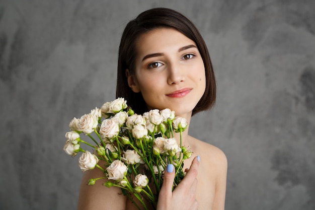 灰色の壁に花を持つ優しい若い女性の肖像画を閉じる