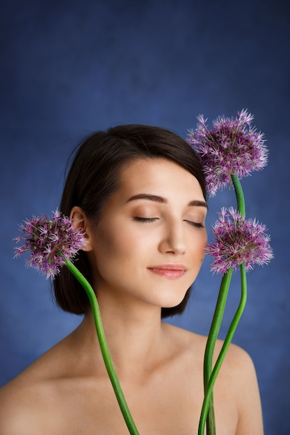 水色の壁にライラック色の花を持つ柔らかい若い女性の肖像画を閉じる