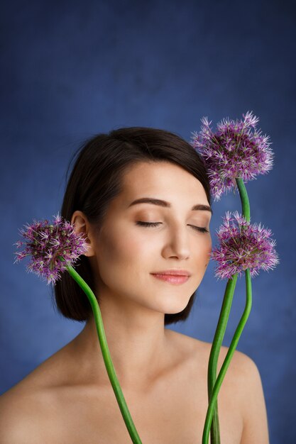 Close up portrait of tender  young woman with lilac flowers over blue wall