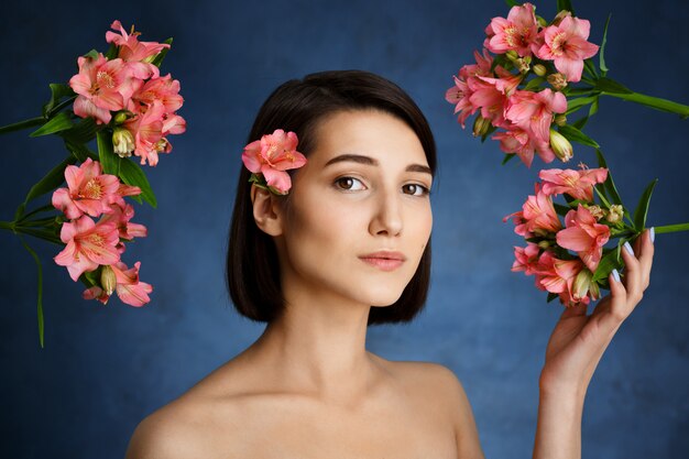 水色の壁にピンクの花を持つ柔らかい若い女性の肖像画を閉じる