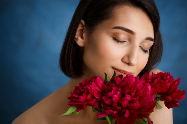 Close up portrait of tender  young woman with red flowers over blue wall