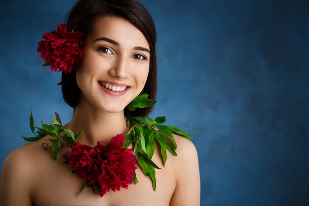 Close up portrait of tender  young woman with red flowers over blue wall