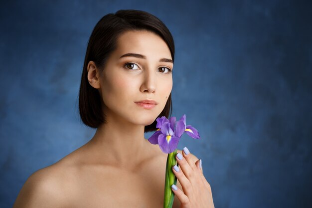 水色の壁に紫のアイリスを持つ優しい若い女性の肖像画を閉じる