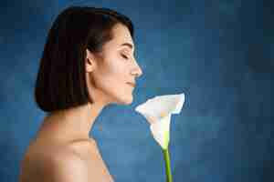 Foto gratuita chiuda sul ritratto di giovane donna tenera con il fiore bianco sopra la parete blu