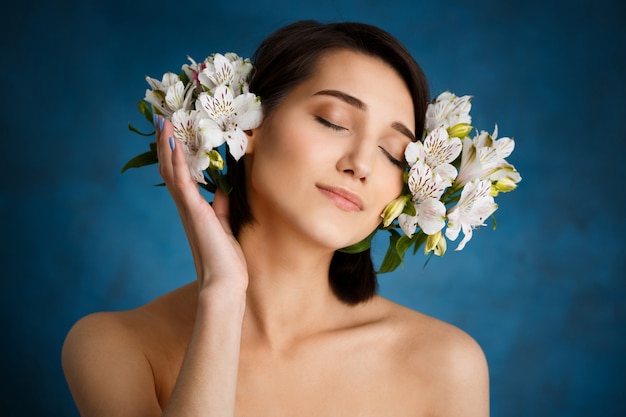 Close up portrait of tender  young woman with white flowers over blue wall