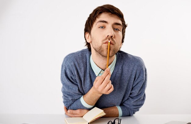 Close-up portrait of thoughtful, handsome male employer, leaning on table, touching lip with pencil as thinking, creating new content, writing-down thoughts