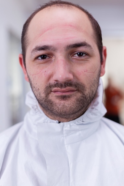 Close up portrait of tired doctor wearing safety protection suit looking on camera during global pandemic with coronavirus