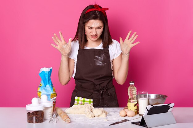 Close up portrait of tired housewife or baker looks sad, spends lots hours preparing Easter cake has, can not make dough desired consistency, wants to stop baking, isolated on pink.