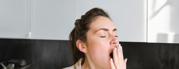 Free photo close up portrait of tired young woman in bathrobe yawning in the morning making herself cup of