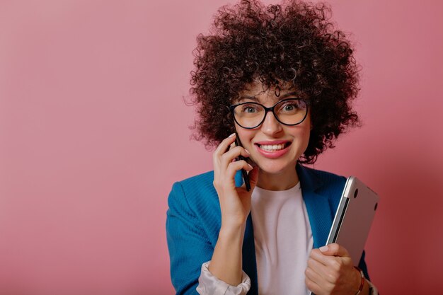 眼鏡をかけてスマートフォンで話している短いアフロヘアスタイルでトレンディなスタイリッシュなビジネス女性の肖像画をクローズアップ