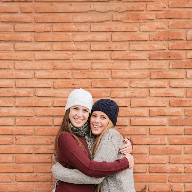 Free photo close up portrait two hugging young women in front of brick wall