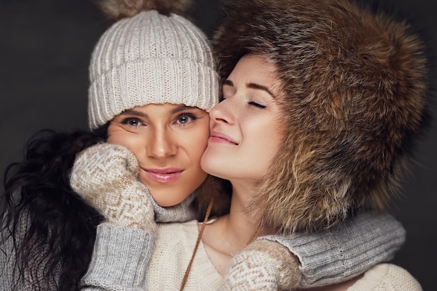 Close up portrait of two positive women wearing warm Christmas hats.