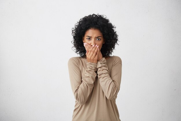 Close up portrait of upset scared black woman, covering her mouth with both palms to prevent screaming sound, after seeing or hearing something bad. Negative emotions, facial expressions and feelings