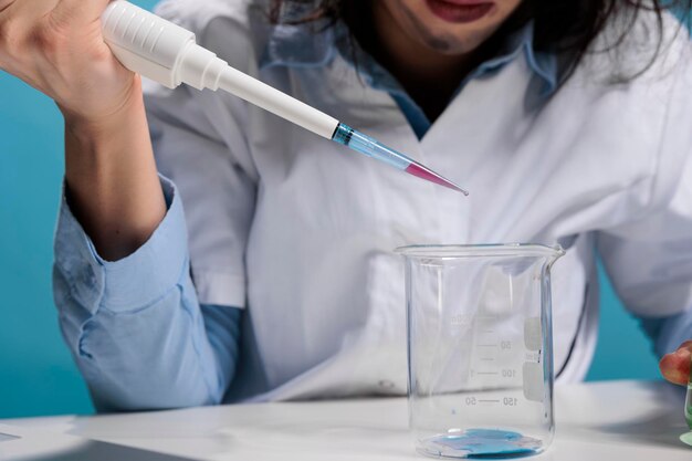 Close up portrait of wacky insane chemist using dropper to mix experimental chemical compounds after lab explosion. Foolish mad looking scientist with pipette doing experiments while sitting at desk.