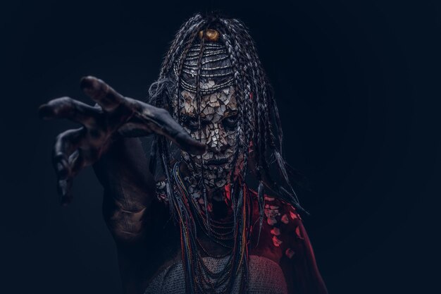 Close-up portrait of a witch from the indigenous African tribe, wearing traditional costume. Make-up concept. Isolated on a dark background.