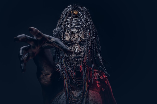 Close-up portrait of a witch from the indigenous African tribe, wearing traditional costume. Make-up concept. Isolated on a dark background.