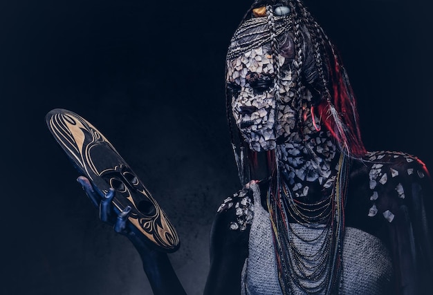 Close-up portrait of a witch from the indigenous African tribe, wearing traditional costume. Make-up concept. Isolated on a dark background.