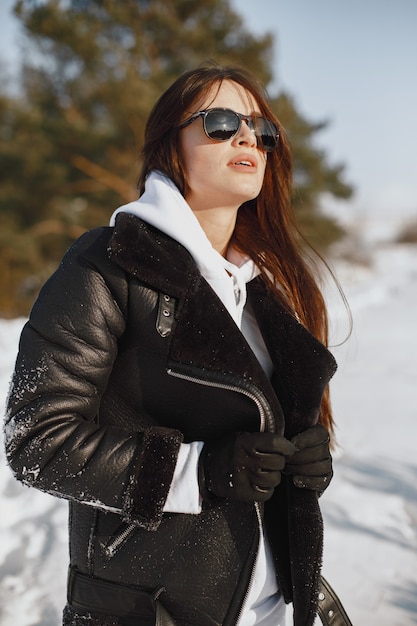 Close-up portrait of woman in black jacket. Woman standing in a forest in snowy day.