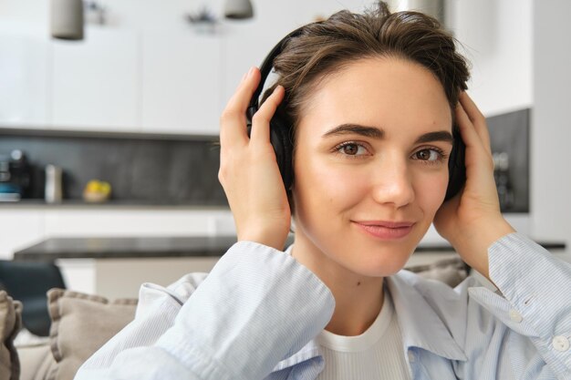 Close up portrait of woman enjoying listening to music in headphones sitting at home on sofa with ea