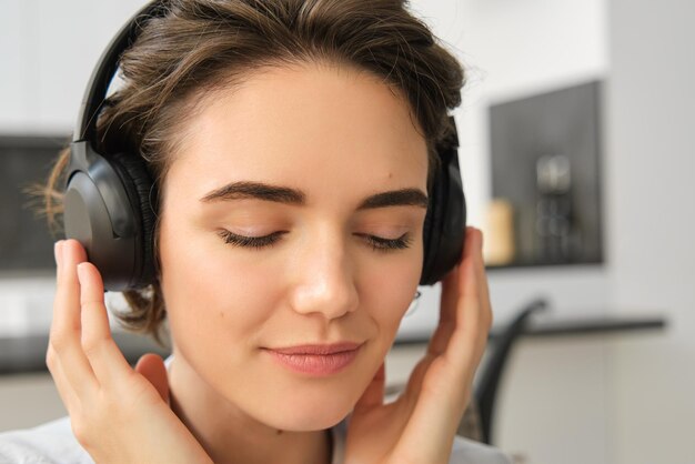 Close up portrait of woman face listening to music in her wireless headphones with delight and