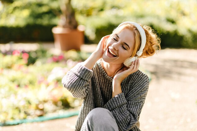 Close-up portrait of woman listening to music in good mood, dressed in gray knitted sweater.