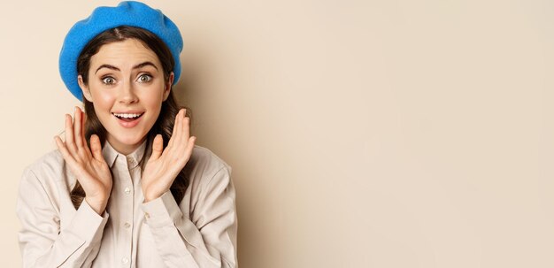 Close up portrait of woman looking surprised amazed reaction at big news special deal standing over beige background