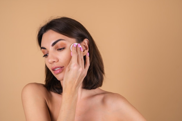 Close up portrait of a   woman with bare shoulders   holding a cotton pad for cleaning her face, beauty portrait, taking care of her face skin