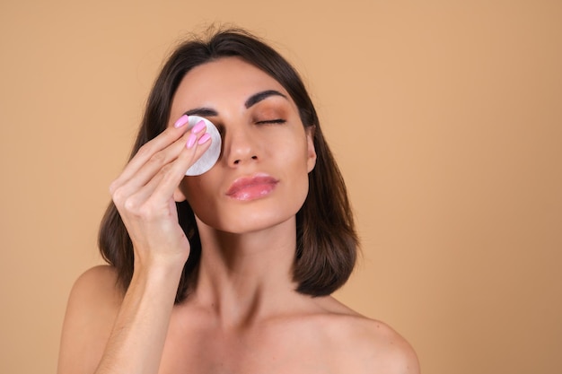 Close up portrait of a   woman with bare shoulders   holding a cotton pad for cleaning her face, beauty portrait, taking care of her face skin