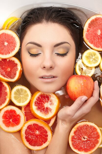浴室で多くのジューシーな柑橘系フルーツレモングレープフルーツを持つ女性の肖像画間近します。