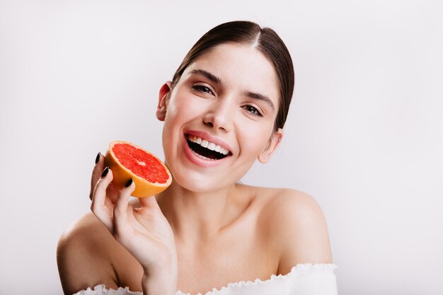 Close-up portrait of woman with perfect clean skin and snow-white smile. Model posing with red juicy citrus fruit.