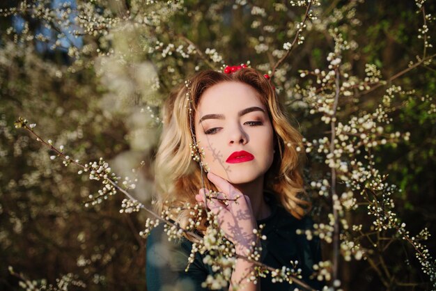 Close up portrait of yong elegance blonde girl at green dress on the garden in spring on blossom trees