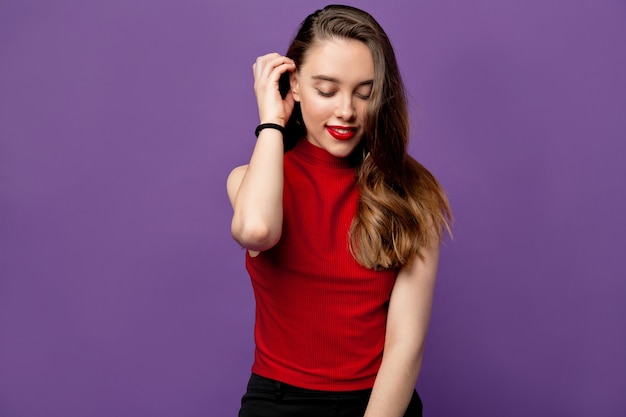 Free photo close up portrait of young adorable  charming attractive brunette girl smiling with shy view and fixes her hairstyle. isolated on purple pastel wall. copy space.