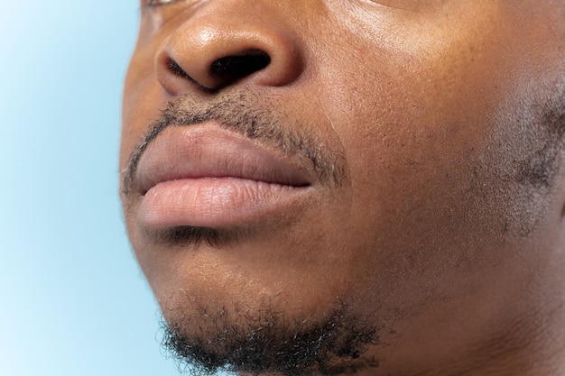 Close up portrait of young african-american man on blue background. Human emotions, facial expression, ad, sales or men's beauty and health concept. Photoshot of lips. Looks calm.