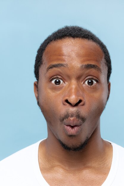 Close up portrait of young african-american man in white shirt on blue wall. Human emotions, facial expression, ad, sales concept.  looks shocked, astonished, wondered.