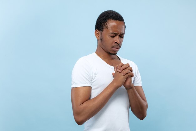 close up portrait of young african-american man in white shirt.. Praying with eyes closed, looks hopeful.