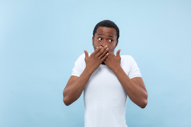 Free photo close up portrait of young african-american man in white shirt.. shocked, covering his mouth by his hands.