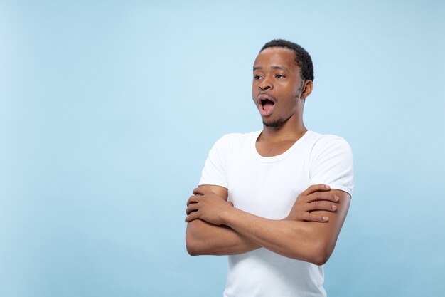 close up portrait of young african-american man in white shirt. Standing hands crossed, shocked and astonished.