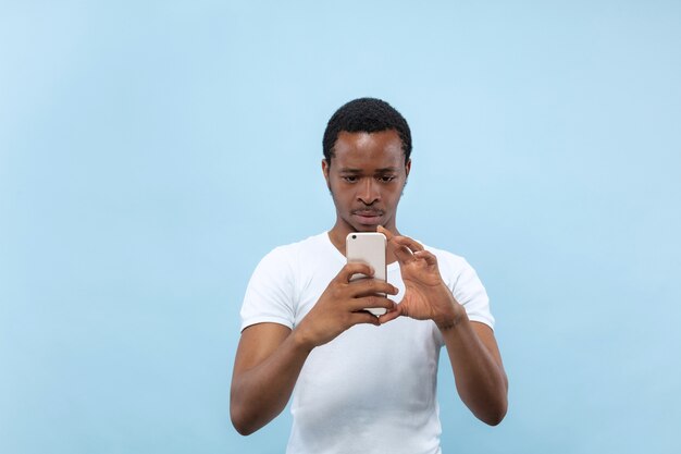 close up portrait of young african-american man in white shirt.. Taking a photo or vlog content on his smartphone.