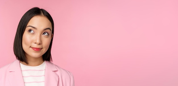 Close up portrait of young asian businesswoman thinking smiling thoughtful and looking at upper left