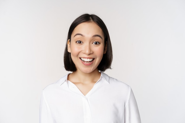 Close up portrait of young asian female model looking amazed at camera smiling white teeth standing against white background