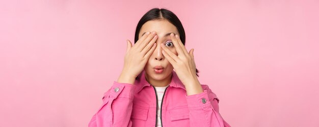 Close up portrait of young asian girl looking surprised express amazement and wonder peeking through