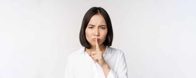 Close up portrait of young asian woman making hush shhh shush sign press finger to lips dont speak keep quiet gesture white background