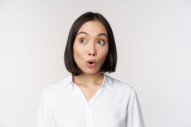 Close up portrait of young asian woman making surprised face looking at upper left corner impressed wow emotion standing over white background