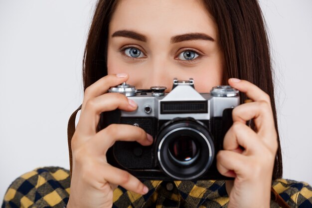 Close up portrait of young beautiful brunette photographer over white wall.
